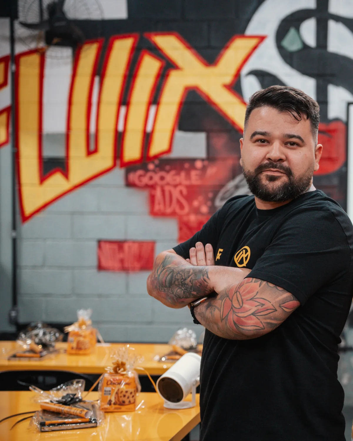 Felipe Jacoto de braços cruzados no escritório do Grupo IX, diante da parede grafitada com a marca Fluix.